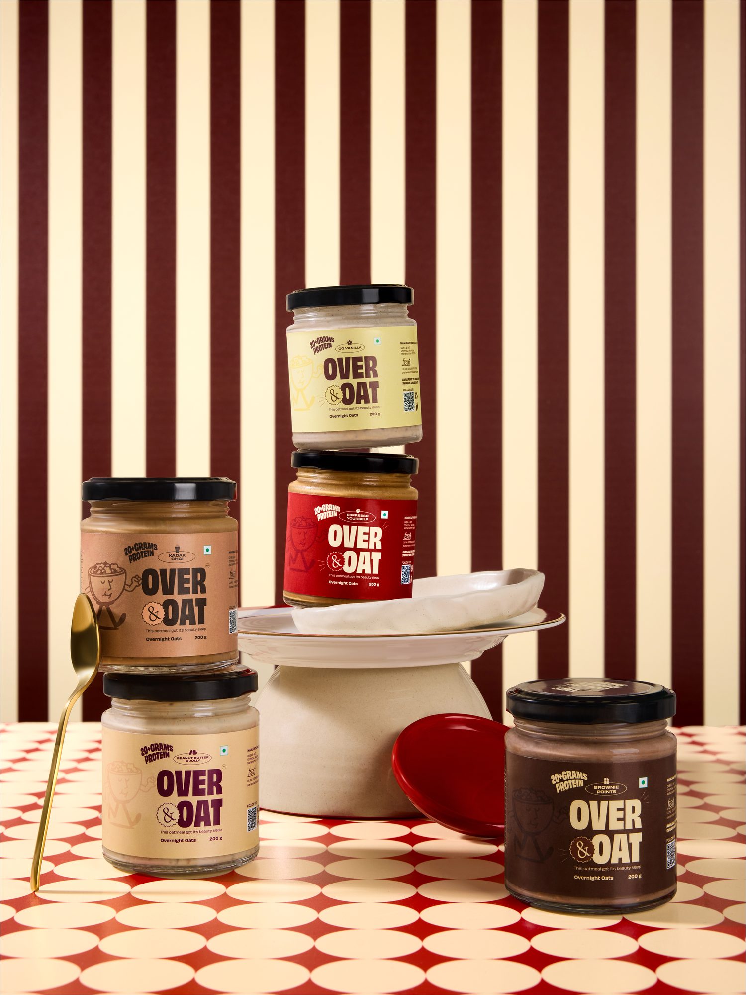Five jars of Over & Oat overnight oats stacked on a cream cake stand against a wine-striped backdrop