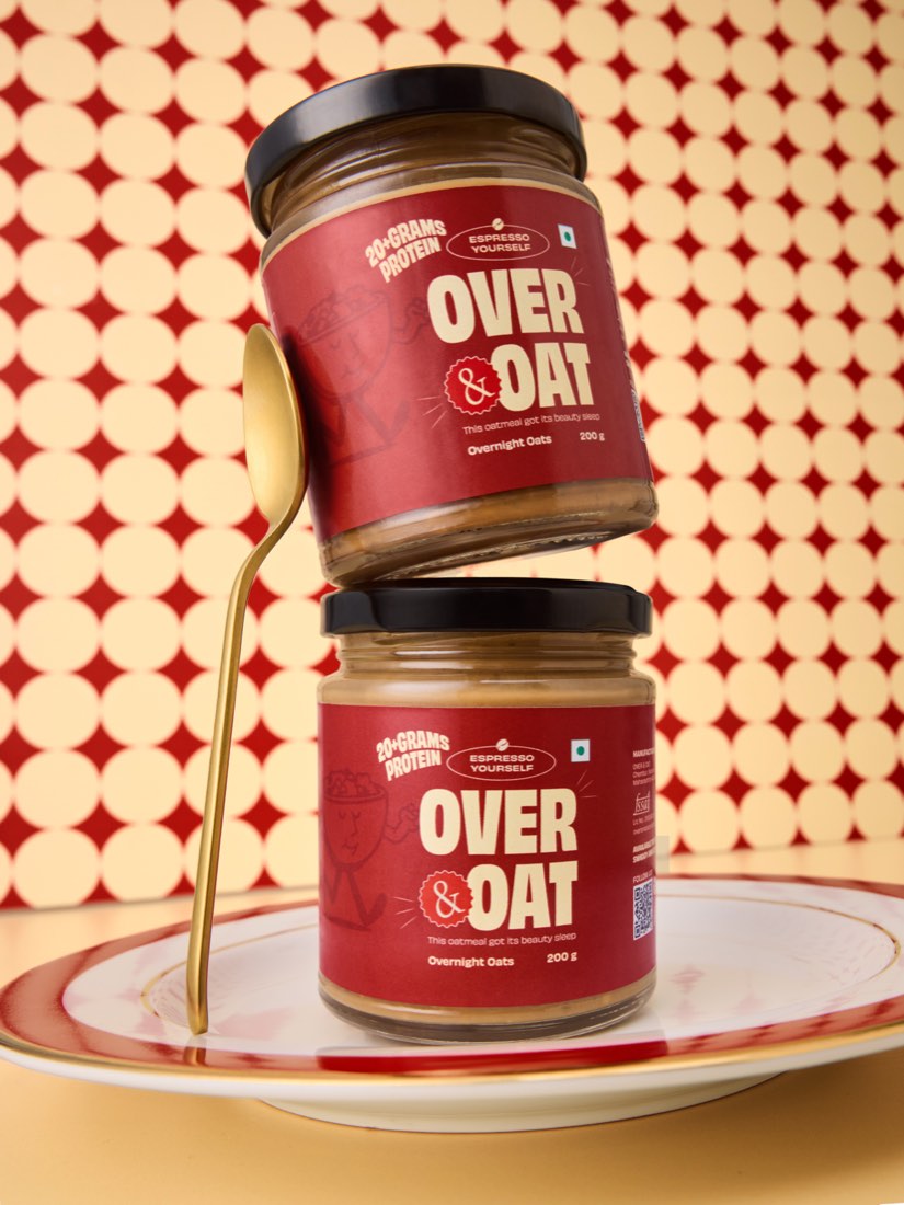 Two stacked jars of Over & Oat Espresso Yourself overnight oats with a gold spoon, on a cream and wine polka-dot set